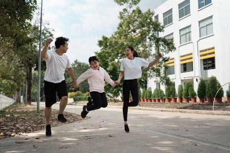 Happy Family Jumping Together Outdoors in Casual Clothing Near Modern Building on a Sunny Dayの写真素材