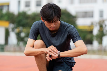Athlete checking performance metrics track field sports urban environment candid shot motivation and focusの写真素材