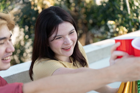 Joyful Friends Celebrating at an Outdoor Party with Red Cups and Laughter in a Sunny Settingの写真素材