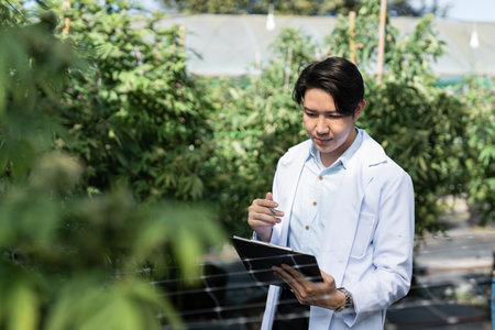Young Scientist Analyzing Data on Tablet in Greenhouse with Lush Green Plants in Backgroundの写真素材