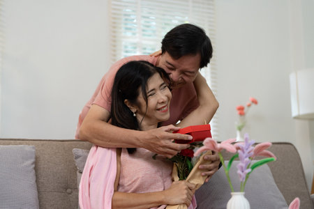 Senior Couple Celebrating Valentines Day with Gifts and Flowers in a Cozy Home Settingの写真素材