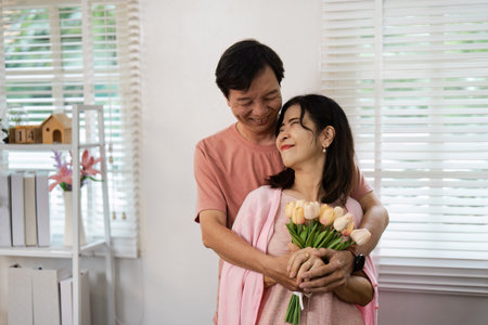 Elderly Couple Celebrating Valentines Day with Flowers and Joyful Smiles in a Cozy Home Settingの写真素材