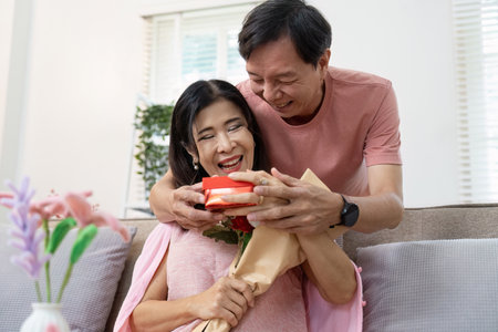 Joyful Senior Couple Celebrating Valentines Day with Gifts and Flowers in a Cozy Home Settingの写真素材