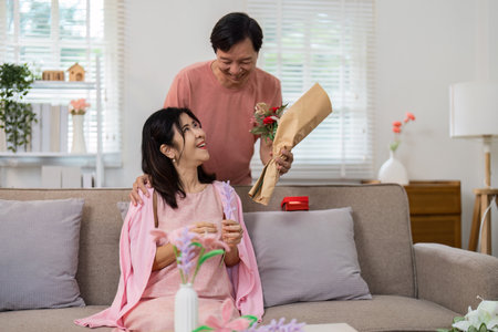 Senior Couple Celebrating Valentines Day at Home with Flowers and Gifts in a Cozy Living Room Settingの写真素材