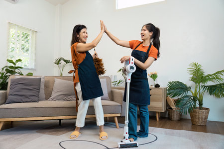 Joyful Housekeepers Celebrating Successful Cleaning in a Modern Living Room with Vacuum and Dusterの写真素材