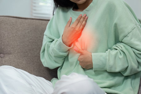 Person Experiencing Discomfort in Chest Area While Sitting on Couch in Casual Clothingの写真素材