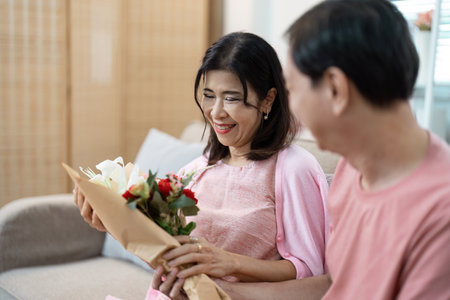 Elderly Couple Celebrating Valentines Day with Flowers and Smiles in Cozy Home Settingの写真素材