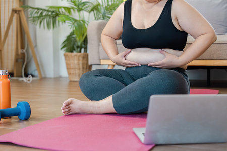 Overweight Individual Engaging in Home Exercise Routine with Yoga Mat and Laptop for a Healthy...