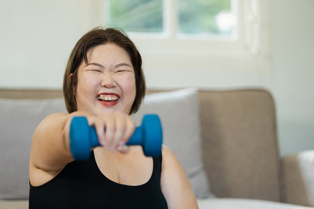 Joyful overweight woman smiling while lifting dumbbells at home, promoting wellness and fitness