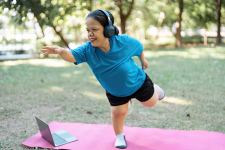 Joyful woman practicing wellness exercises with online guidance in a park, focusing on balance and...