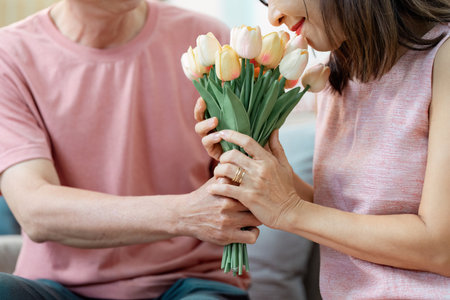 Senior couple sharing a tender moment with a bouquet of tulips on Valentines Day in their cozy living roomの写真素材