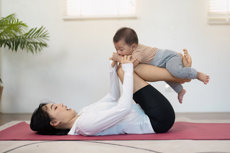 Multitasking mother playfully lifting her baby while exercising, creating joyful moments at homeの写真素材