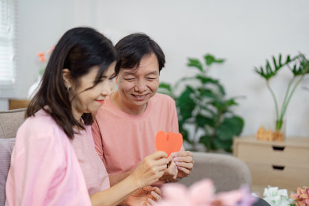 Senior couple exchanging heartfelt messages with love notes on Valentines Day in their living roomの写真素材