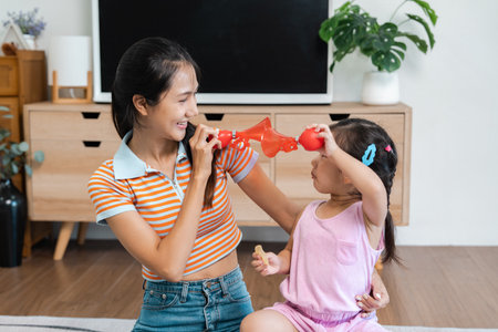Mother and toddler playfully using toy horns, creating joyful family fun at homeの写真素材