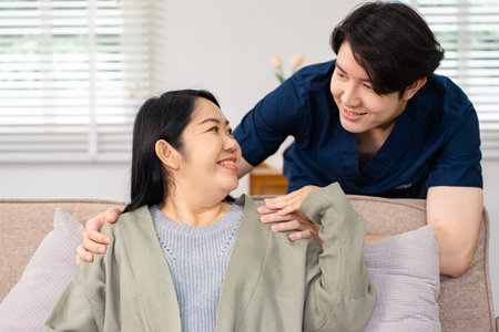 Friendly healthcare professional providing comfort and reassurance to a smiling patient during an in-home visitの写真素材