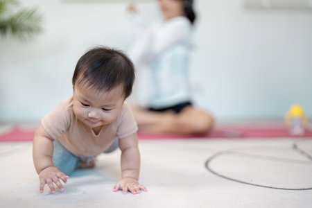 Curious baby crawling on the mat while mother exercises in the backgroundの写真素材