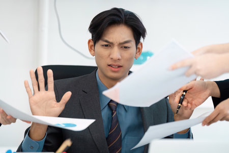 Overwhelmed businessman rejecting excessive paperwork in a busy office.の写真素材