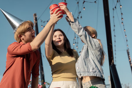Excited friends raising red cups in a toast outdoors, wearing party hats and celebrating together in a festive atmosphere.の写真素材