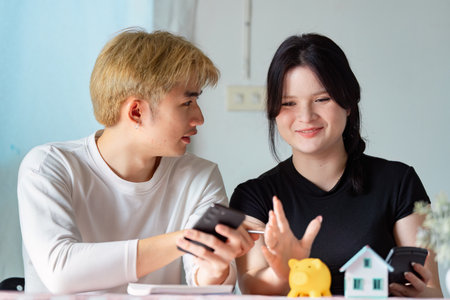 Young couple enthusiastically discussing real estate plans with a piggy bank and mobile devicesの写真素材