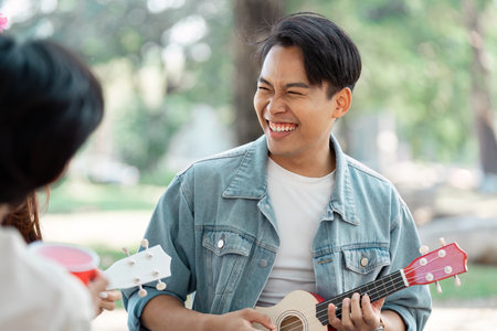 Diverse young man playing ukulele and laughing with friends in a park.の写真素材