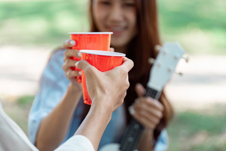 Friends toasting with red cups during a picnic in a park setting.の写真素材