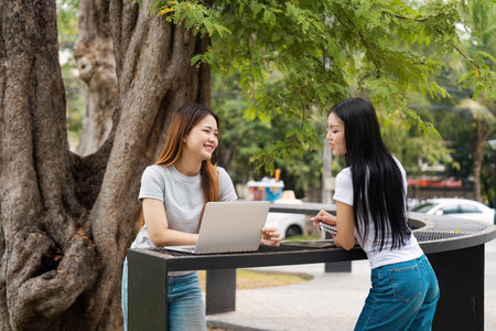 Diverse female students discussing study material outdoors by a tree.の写真素材