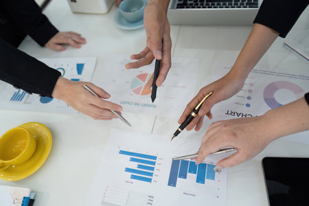 Hands of diverse professionals analyzing financial charts during a business meeting.の写真素材