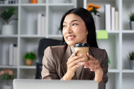 Cheerful businesswoman holding a coffee cup and smiling in a modern officeの写真素材