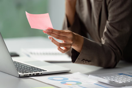 Businesswoman reviewing notes while holding a sticky note in a modern officeの写真素材