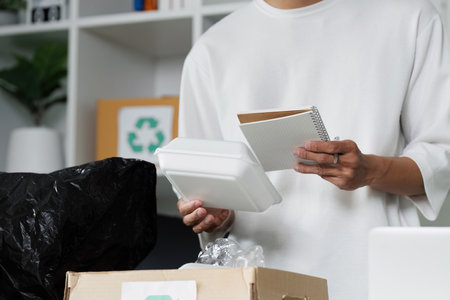 Person recycling packaging materials and organizing notes in a sustainable workspace, promoting...