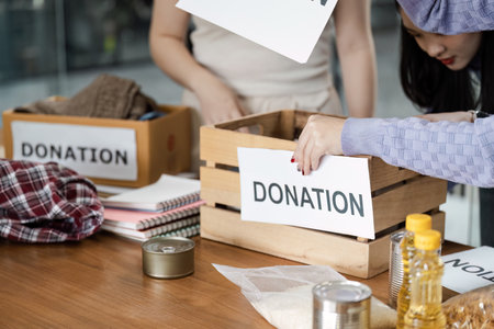 Individuals sorting items into donation boxes labeled for community support, organizing food and...