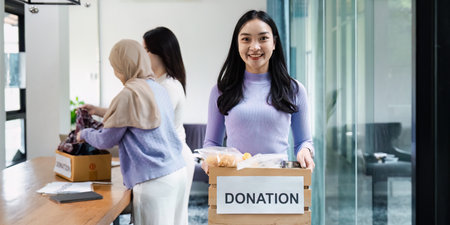 Volunteer smiling while holding a donation box at a community event, collecting food and clothing for those in need.の写真素材