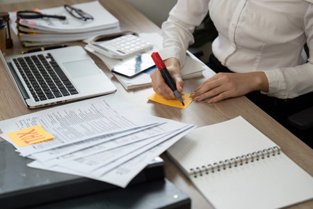 Accountant organizing tax documents and notes at a desk with a laptop and calculator.