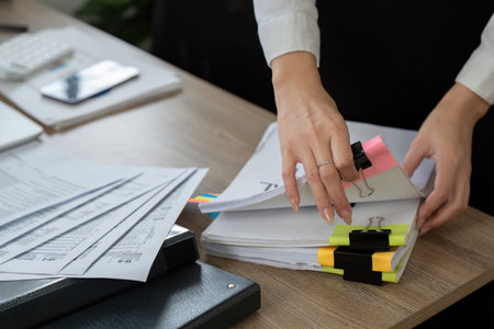Professional accountant organizing financial documents on a desk with colorful clips and reports.