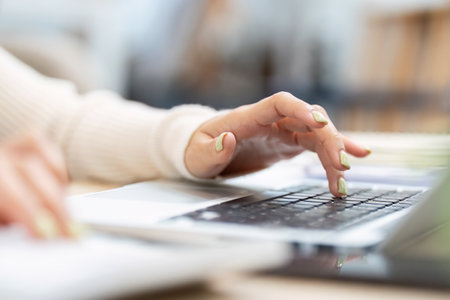 Close-up of a woman typing on a laptop keyboard in a modern office environment.の写真素材