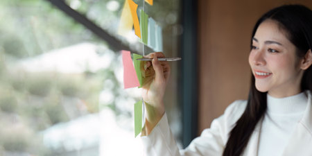 Female professional writing on sticky notes while brainstorming ideas in a modern office setting.の写真素材