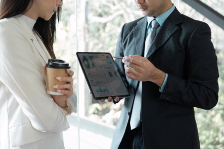 Business professional presenting data on a tablet while another holds a coffee cup, discussing insights.の写真素材