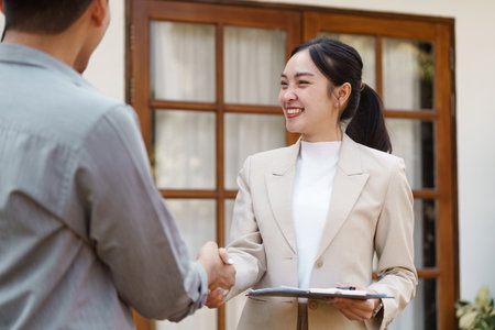 Finalizing the sale. Agent shaking hands with buyers in front of the house.の写真素材