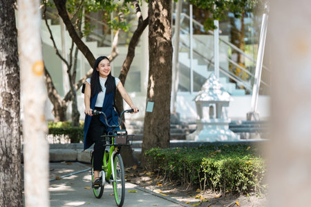 Eco-friendly transportation. Young woman riding a green bicycle through a park, promoting sustainable commuting and active lifestyle.の写真素材