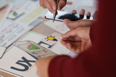 Exploring Ideas in UX UI Design. Hands holding a creative lightbulb symbol during a collaborative design discussion.の写真素材