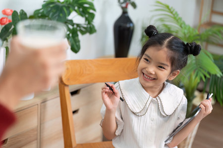 Excitement and Motivation. A girl happily engages in learning as her mother supports her education.の写真素材