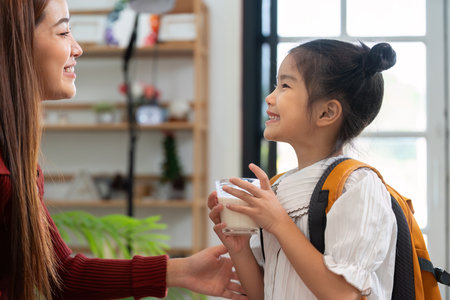 Breakfast and School Readiness. A young girl enjoys a nutritious drink while preparing for her school day with her mother.の写真素材