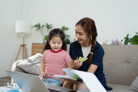 Engaged mother enjoying a creative moment with her daughter while working from home.の写真素材
