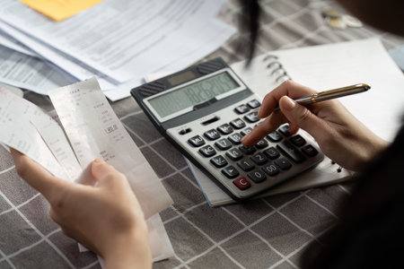 Individual calculating expenses using a calculator and receipts on a tableの写真素材