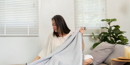 Wellness Routine and Elderly Care. A woman enjoys her cozy space as she arranges a blanket thoughtfully.の写真素材