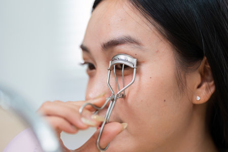 Skincare and Empowerment. A woman uses an eyelash curler to enhance her natural beauty and boost her confidence.の写真素材