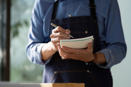 Diligent small business owner making notes in a notebook while managing tasks in a startup workspace for e-businessの写真素材
