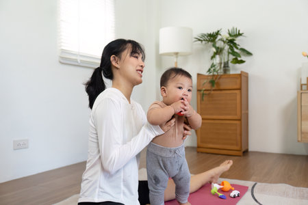 Support and Learning. A mother supporting her standing baby, emphasizing nurturing moments in play and development.の写真素材