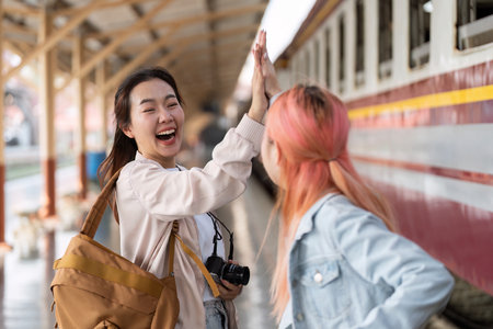 Friendship and Travel. Two friends share a joyful moment at the train station, celebrating their journey together.の写真素材