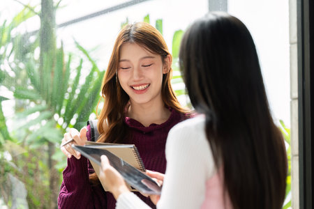 Friendship and College Life. Two students share a joyful moment with a notebook in hand, capturing...